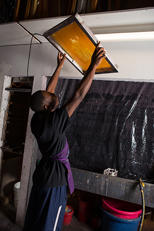 A student holds a silkscreen up to the light to check that it is clean. He checks to see if there are any holes in the image on the screen still clogged with ink.
