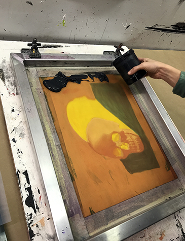 This is an image of a silkscreen with a human skull on it. Black ink is being applied to the top of the silkscreen.