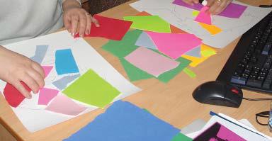 This image shows students' hands arranging various multi colored pieces of paper into a composition.