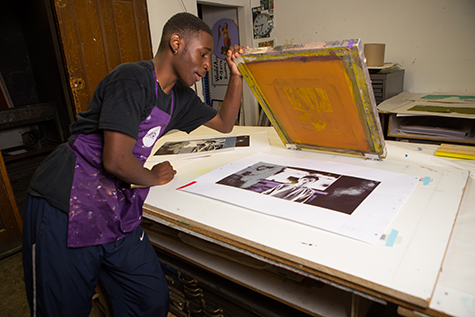 A student lifts a screen to reveal a recently-made print