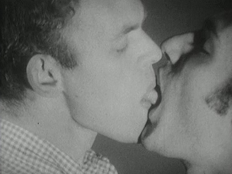 A black and white film still of two men kissing passionately.
