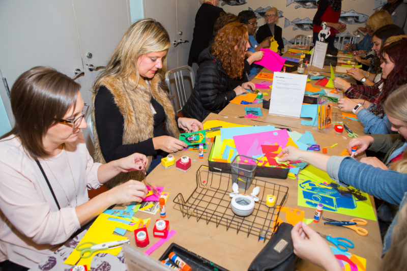 Group of teachers sitting at a table, cutting paper and collaging colorful paper.