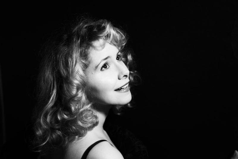 A black and white photograph of a woman with light hair smiling and looking off to the right of the frame.