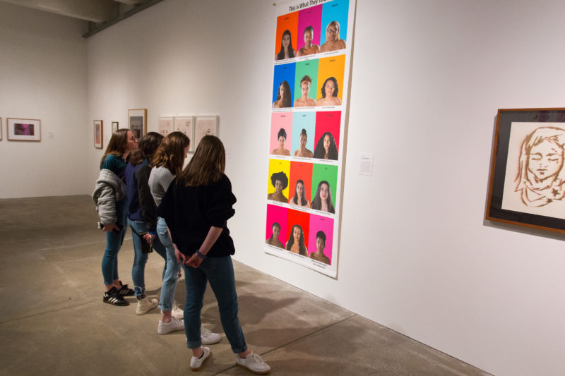 A group of girls stand together to look at large artwork on gallery wall.