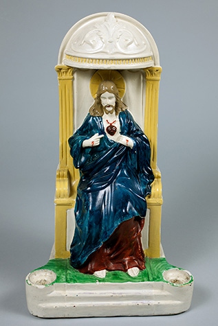 Statue of Jesus sitting on an ornate throne in a blue robe with an exposed heart and bleeding wounds on his hands.