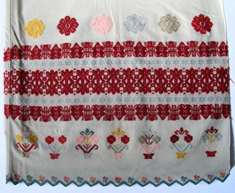 Full-view of embroidered tablecloth. The tablecloth is white with predominantly red accents.