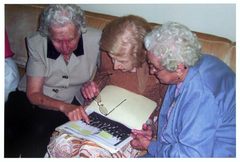 Three women huddled around an image, working to identify who is in a photo.