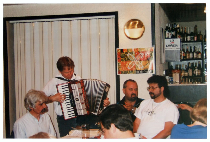 A man with brown hair plays accordion amid an intimate audience.
