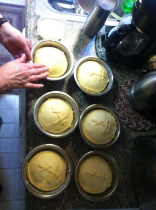 Photo of hands making a loaf of paska, next to five more loaves of paska, in dough form, ready to be baked.