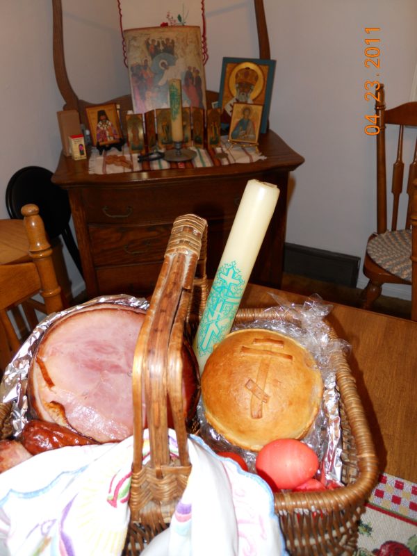 Photo of a baked loaf of paska inside a basket with meats and Easter eggs.