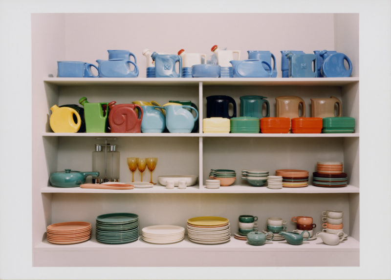 A collection of dishware called Fiestaware is displayed on four shelves. Plates, bowls, creamers, cups, pitchers, and wine glasses make up the collection.