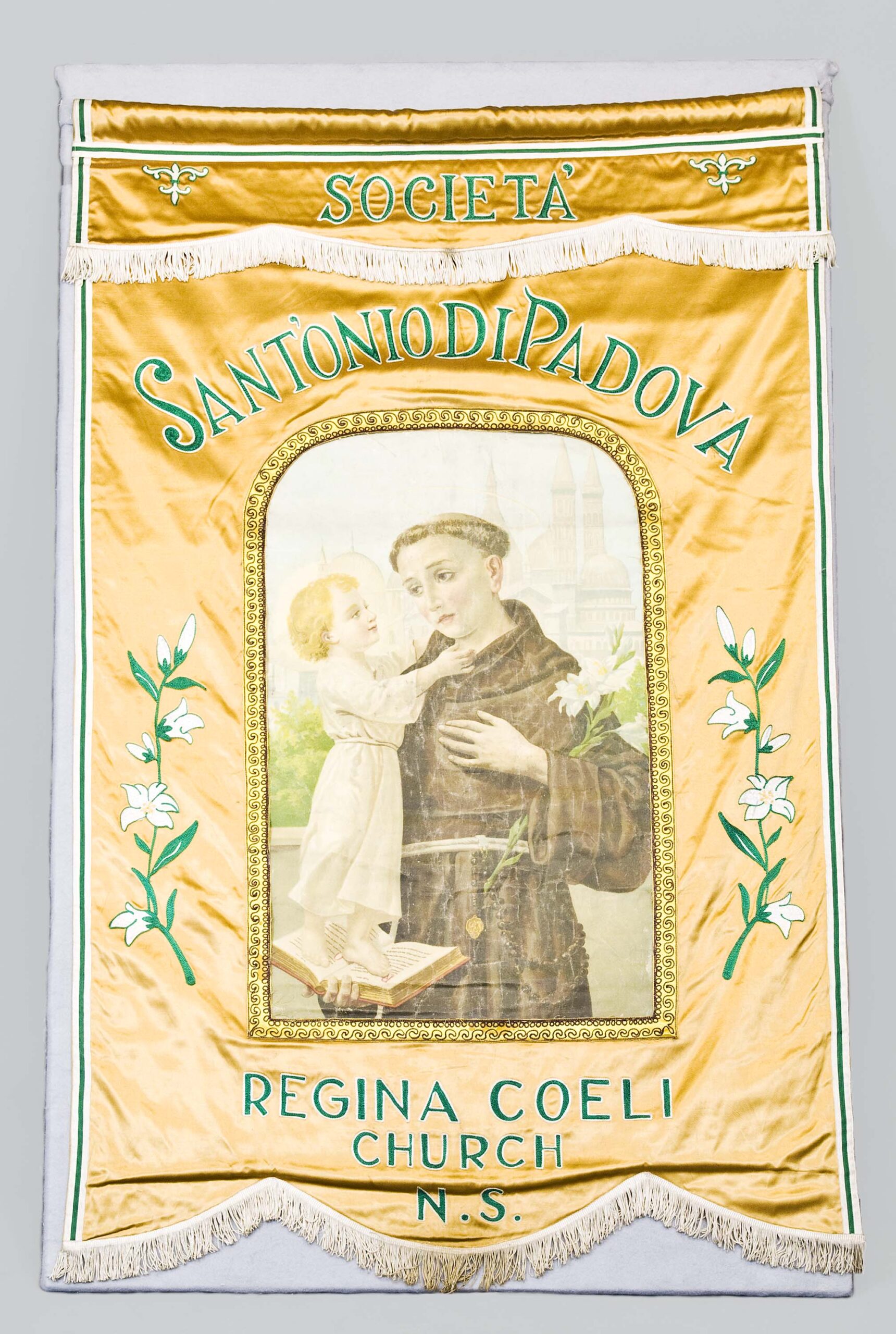 Front view of a banner featuring San Antonio and a young child. The banner is yellow with green, white, and gold accents. The banner also features the name of a church written in Italian.