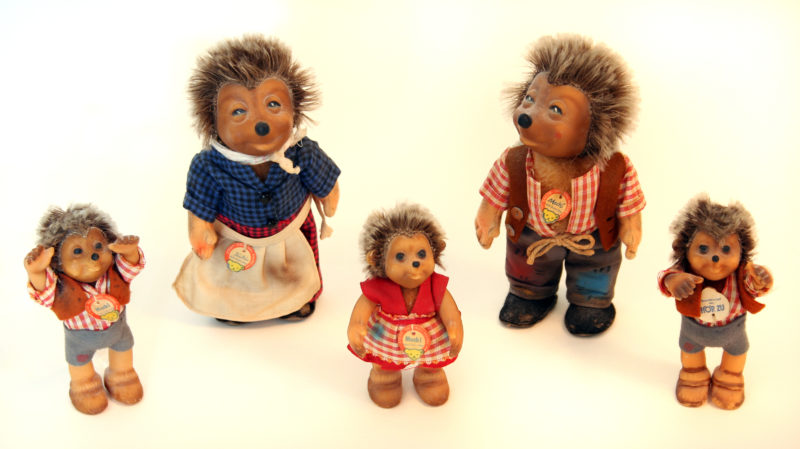 A family of Steiff toy hedgehogs. Two parent hedgehogs and three children figurines smile, stand up-right and wear human clothing