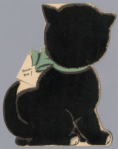 Back of a greeting card in the shape of the back of a seated kitten, with fuzzy black flocking. The kitten has a blue bow around its neck with tag that says “Goodbye!”