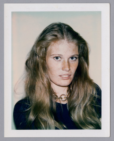 A Polaroid of a woman with long, light brown hair and blue eyes wearing a large gold link necklace and a dark blue top.