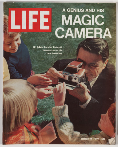 The cover of Life magazine from October 27, 1972 has the headline “A Genius and his Magic Camera” and shows a man with brown hair and a dark suit using a Polaroid camera. He is surrounded by several children who are reaching out to grab the photo emerging from the camera. The caption reads, “Dr. Edwin Land of Polaroid demonstrates his new invention.”