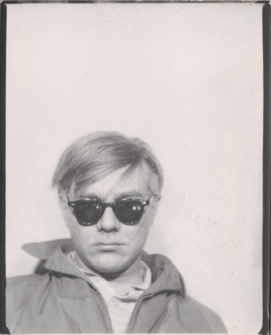 This is a single black and white photo from a photo strip taken in a photobooth. This is a self-portrait of Andy Warhol wearing sunglasses and a jacket with a popped up collar.