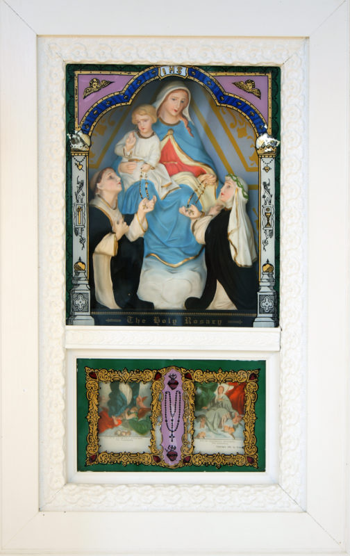 Front view of a Virgin Mary Vitrine depicting Mary holding baby Jesus with two people kneeling next to her.