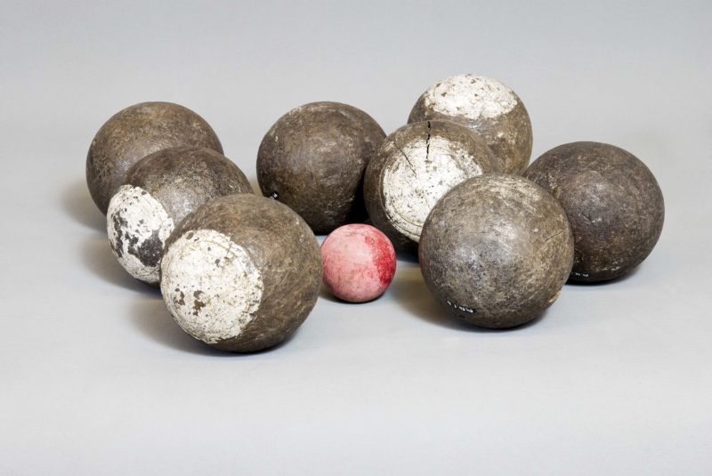 Front view of eight worn bocce balls—seven regular bocce balls, and one boccini or “jack.”
