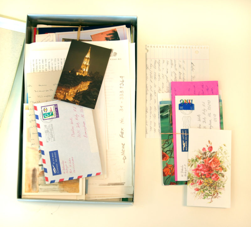 Overhead view of an opened box of letters. The box is full of letters and postcards, with some extracted letters laying outside of the box.