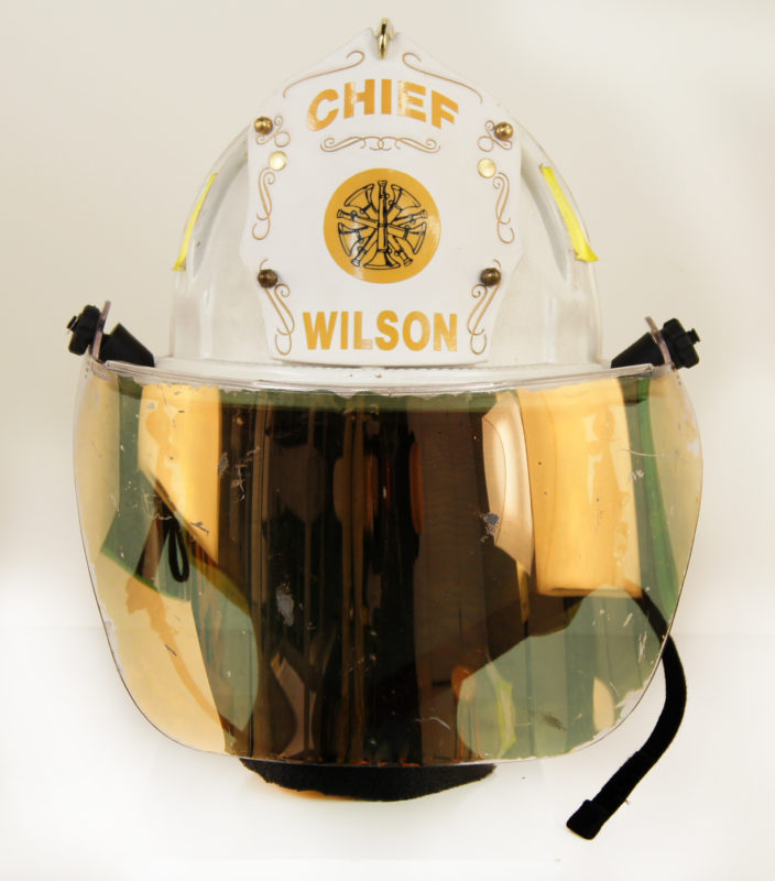 Front view of Fire Chief Lamonte E. Wilson’s firefighter helmet with attached visor. The helmet reads “Chief Wilson” and is embroidered with gold designs.