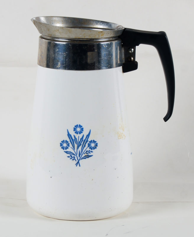 Close-up view of metal coffee pot. The coffee pot is white and has the CorningWare logo and a blue floral design.