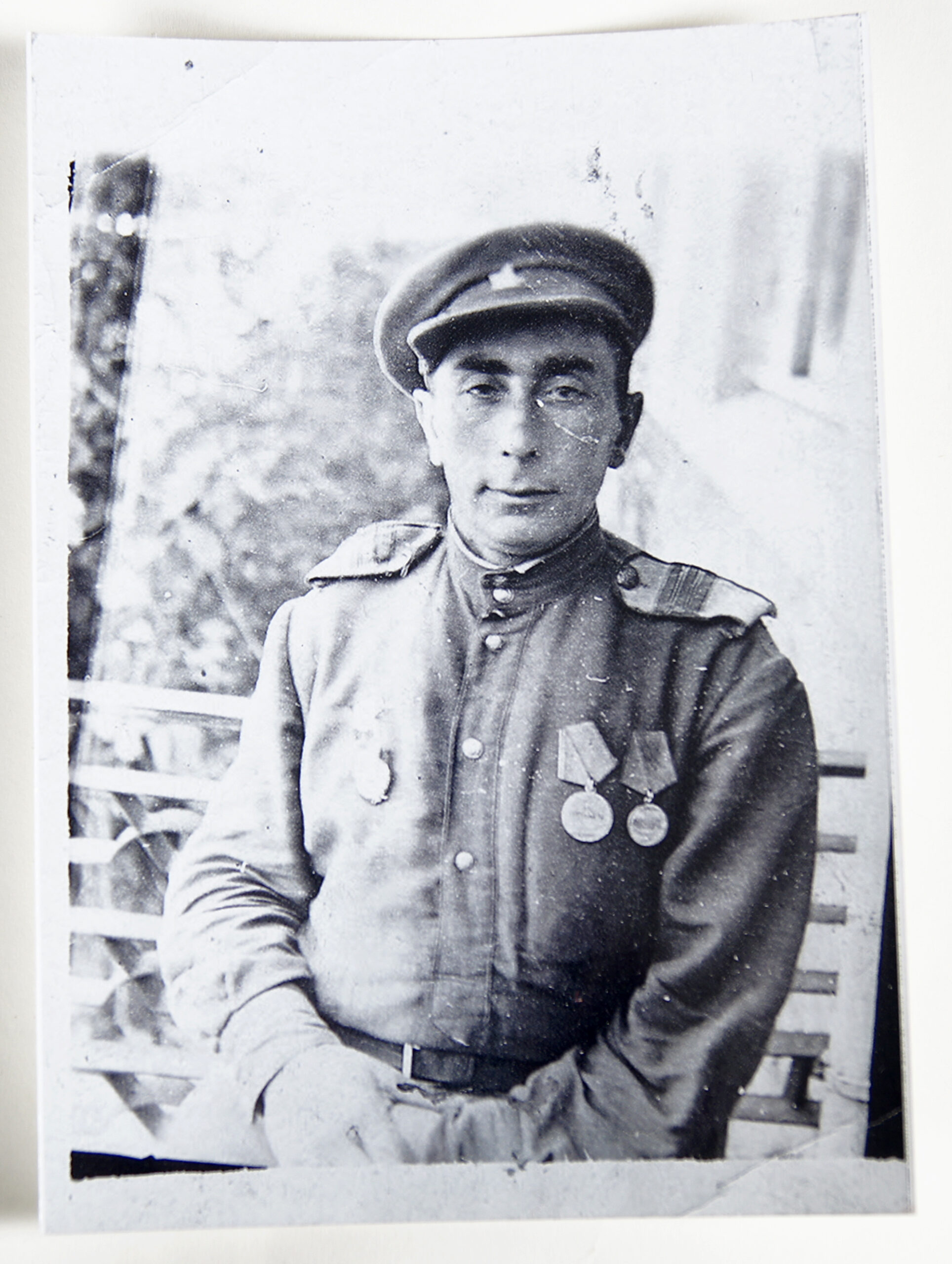 View of black and white photograph. A man in uniform, adorned with three medals, looks at the camera.