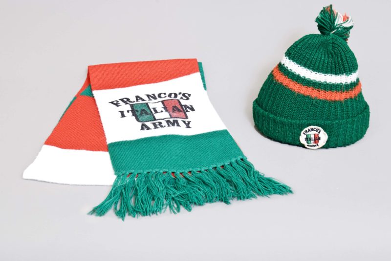 Front view of a folded Franco’s Italian Army scarf with logo, next to a Franco’s Italian Army sock-cap.