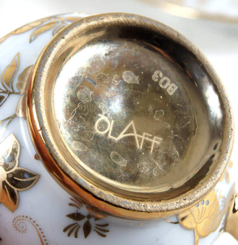 View of underside of a piece of a tea set. The underside is painted gold and reads “OLAFF.”