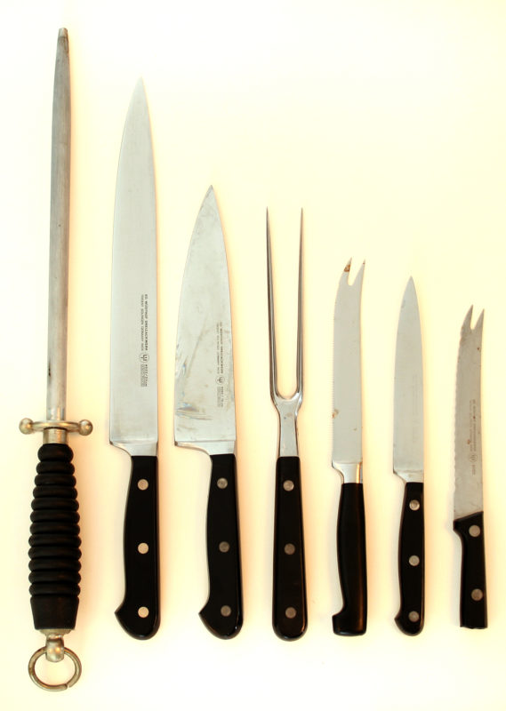 Front view of a set of seven knives of different sizes with black handles. The knives are organized by size in descending order from longest to shortest.