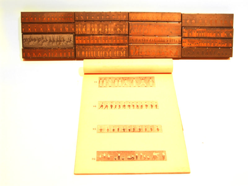 Front view of letterpress blocks depicting images of bodies in motion. Placed in front of the blocks is a yellow piece of paper with examples of four printed images.