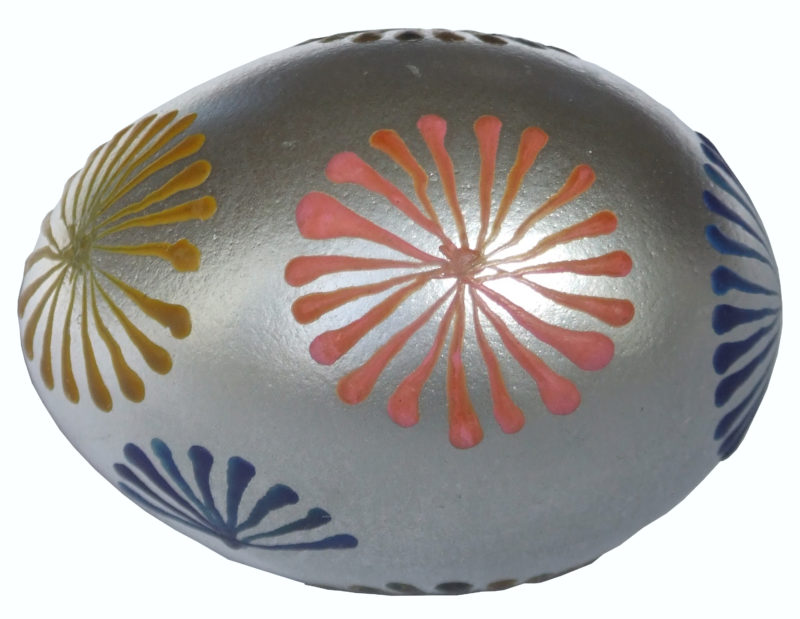 Front view of pysanky egg laid horizontal. The egg is silver and features navy, pink, and yellow accents in a bloom-like design.