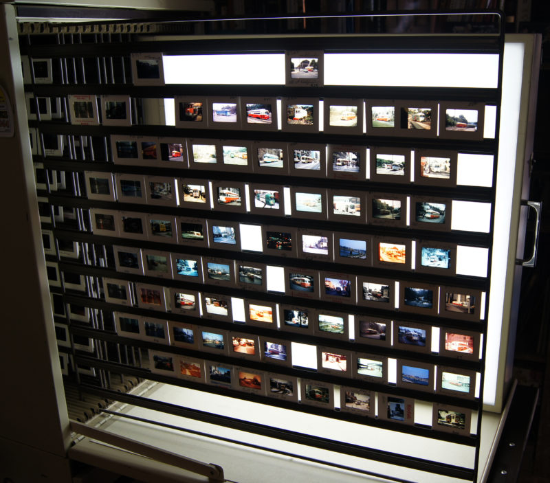 Front view of a slide cabinet filled with slides of varying, colorful scenes. The slides are placed on a rack that extends outward and can be pushed in to close.