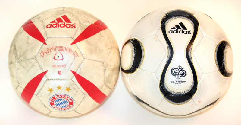Front view of two white Adidas soccer balls. The soccer ball on the left has red design accents and the soccer ball on the right has black design accents.