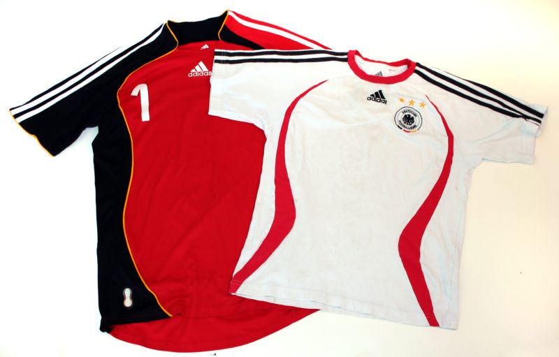 Front view of two soccer jerseys. A white jersey with black, yellow, and red accents overlaps a referee’s jersey.