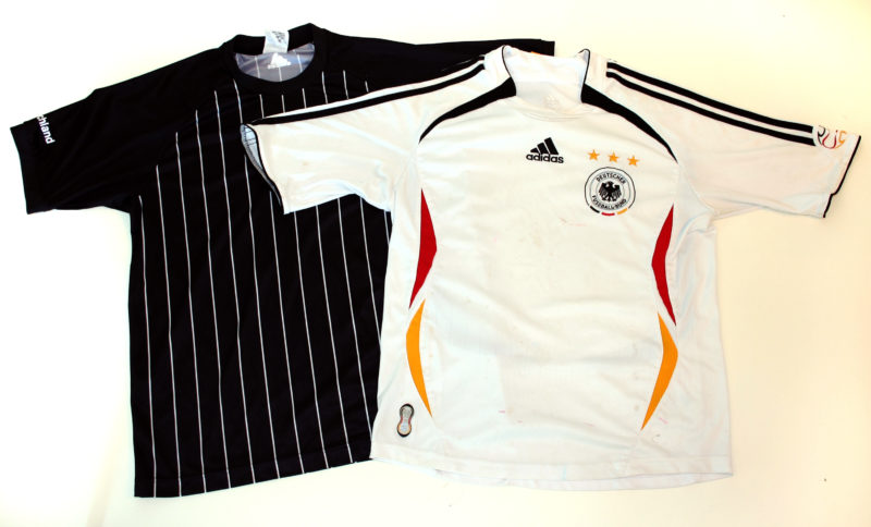 Front view of two soccer jerseys. A white Adidas jersey with red, black, and yellow accents overlaps a larger red Adidas jersey with black, white, and yellow accents.