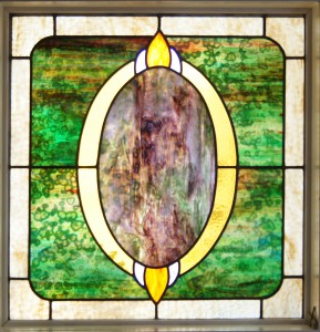 Front view of a stained glass window. The window features a green-gradient square and a yellow “O” shape in its center.