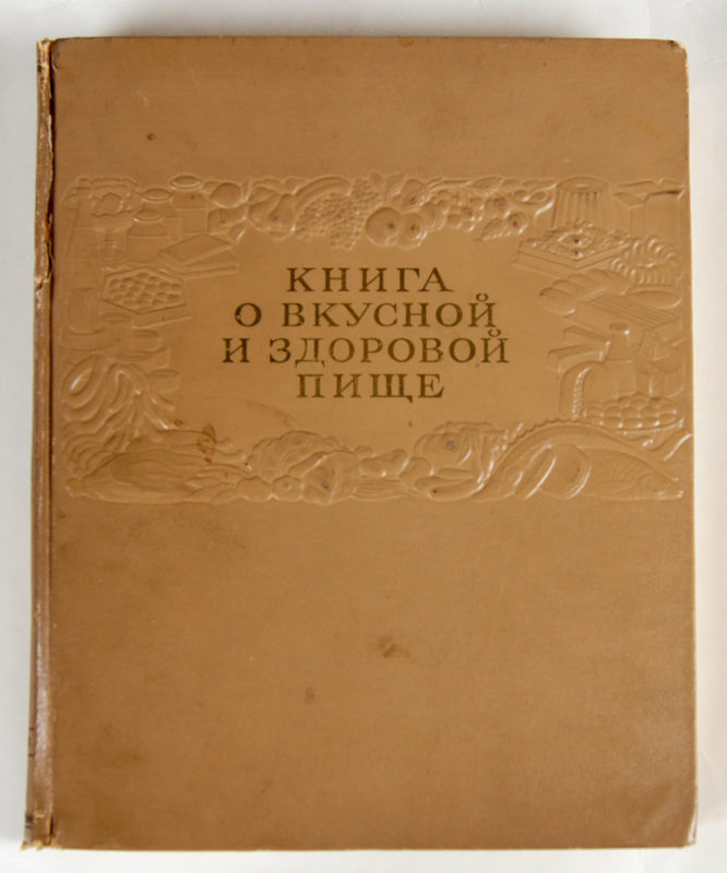Front view of cookbook cover. The cover is brown with a decorative, textured protrusion in the shape of various foods surrounding the title.