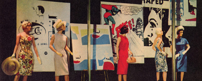 A department store display window featuring five women mannequins in various poses and styles of dress. In the background are five panels of artwork by Andy Warhol taken from various newspaper advertisements and comics; including an image of Superman in a red cape with the word “PUFF!” in large, red lettering.