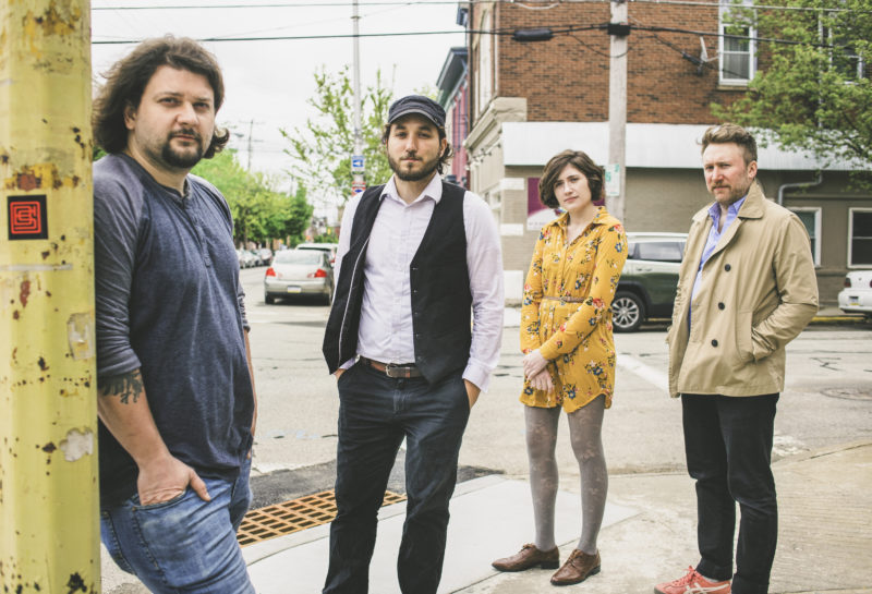 Four people stand on a street corner, facing the camera.