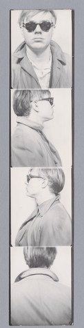 Black-and-white photobooth strip showing four images of Andy Warhol. First is a portrait of him facing the camera, unsmiling, wearing dark sunglasses, and a light colored overcoat over a white shirt. The second is of him in profile, facing right, wearing the same sunglasses and overcoat. The third is of him in profile facing left. The fourth image is of him with his back to the camera.