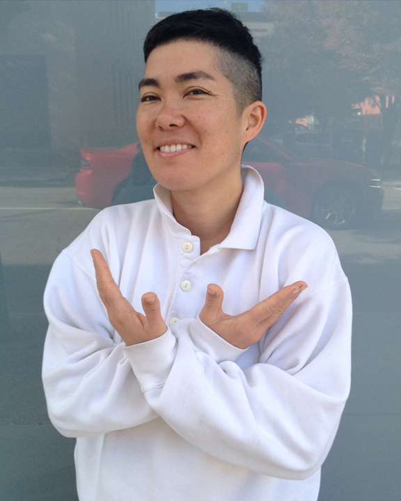 Smiling person in a white rugby shirt crosses their hands in front of a street scene.