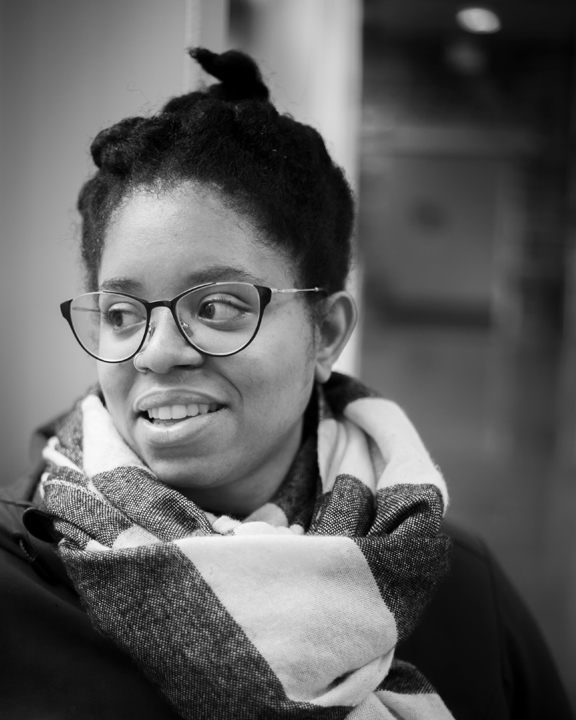 Person in glasses and a scarf looks off to the left in black and white.