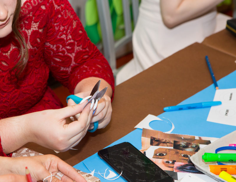 A person is sitting at a table cutting paper with scissors.