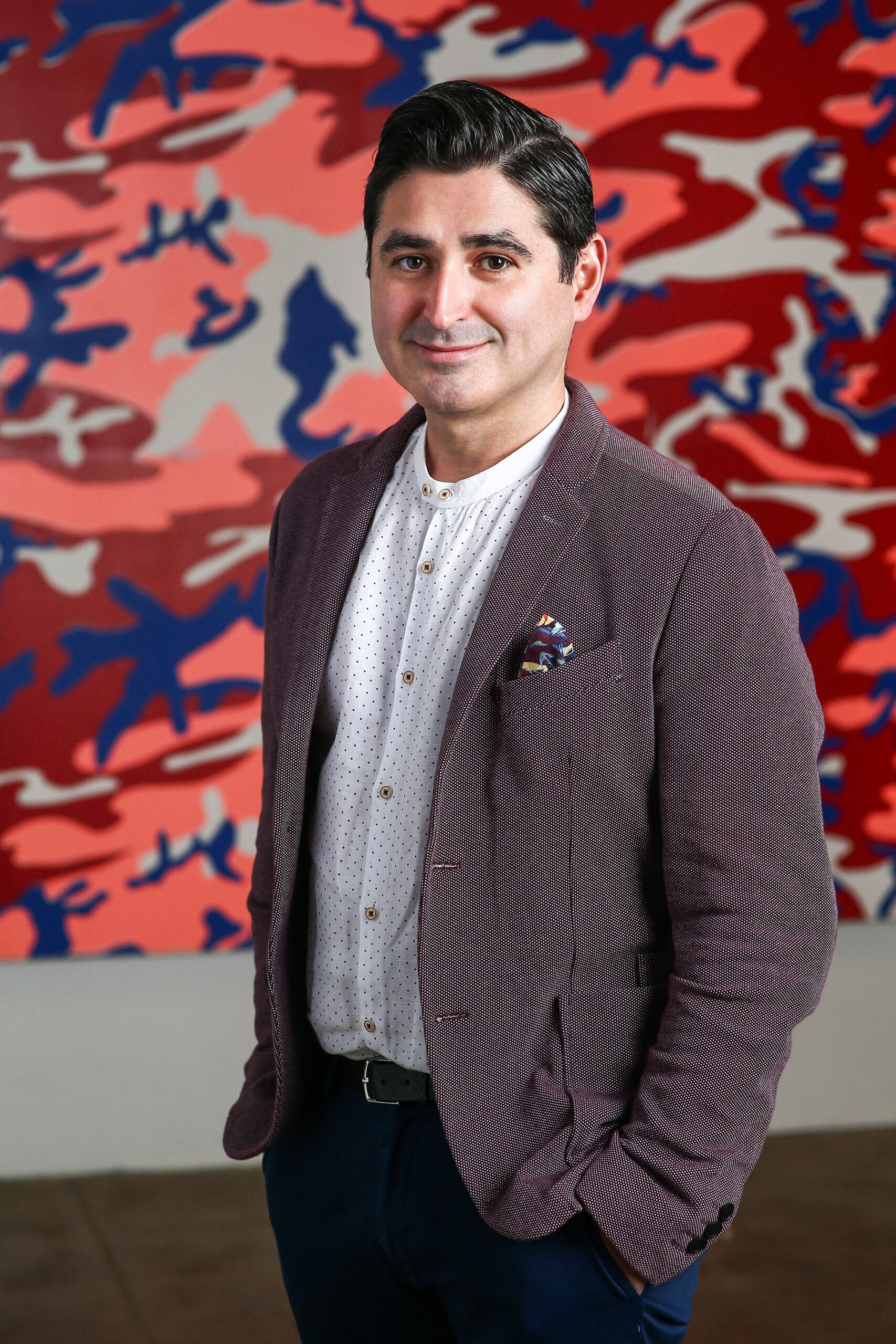 Man stands in front of colorful Warhol camouflage painting.