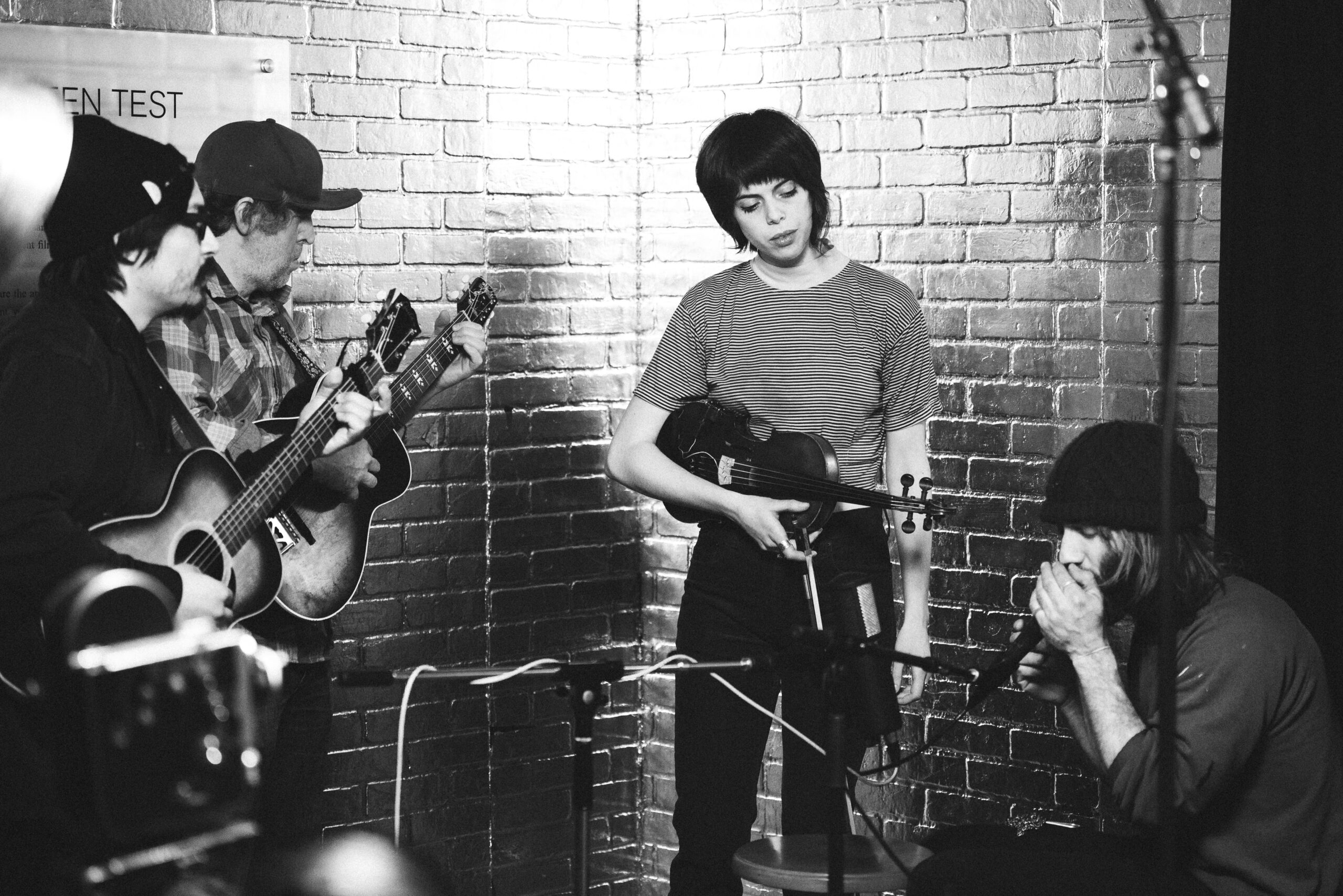 A four-piece band performs a set against a backdrop of silver bricks.