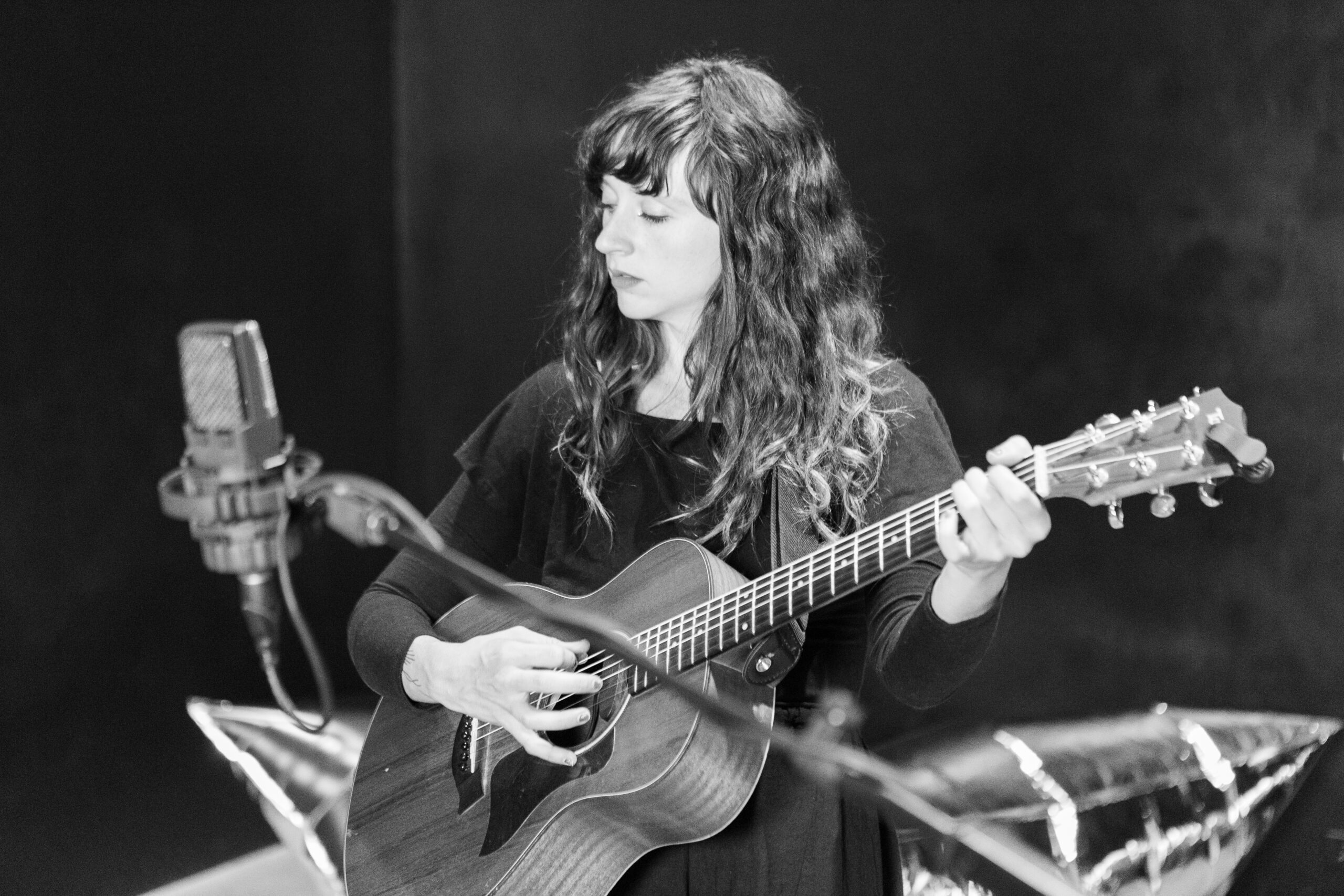 Woman playing guitar in the foreground of a studio session.
