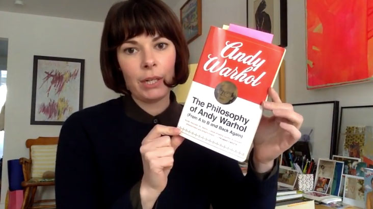 Woman holds book, her apartment in the background.