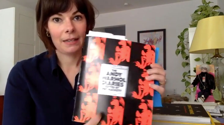 Woman holds book, her apartment in the background.