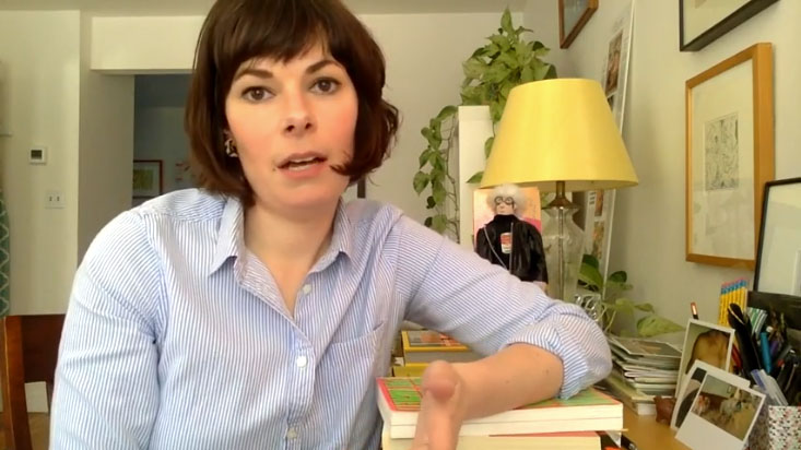 Woman holds book, her apartment in the background.